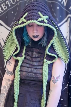 a woman with blue hair wearing a crocheted hat and green braids on her head