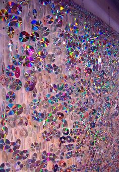 many cds are hanging on the wall in front of a window with iridescent colors