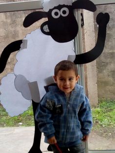 a young boy standing next to a cut out of a sheep