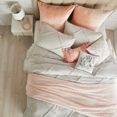 a bed with pink and grey pillows on top of it next to a night stand