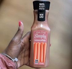 a hand holding a bottle of hot dog simply smoothie with orange sticks in it