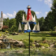 a red and white light house sitting on top of a lush green field next to a pond