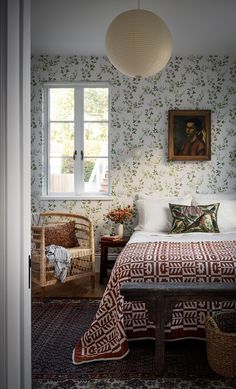 a bed sitting under a window next to a painting on the wall in a bedroom