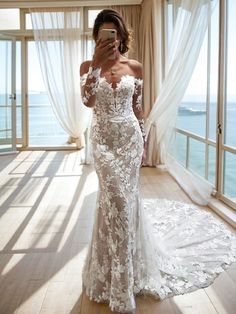 a woman in a white wedding dress taking a selfie with her cell phone by the window