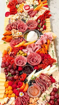 an assortment of meats and cheeses on a long platter with grapes, tomatoes, olives, nuts, bread