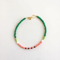 the bracelet is made with green, pink and white beads on a gold plated chain