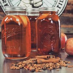 three jars filled with liquid sitting on top of a table next to apples and cinnamons