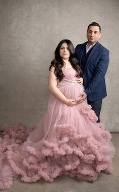 a pregnant woman in a pink dress standing next to a man wearing a blue suit