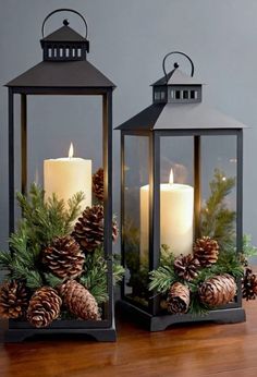 two black lanterns with pine cones and evergreens on them are sitting on a table