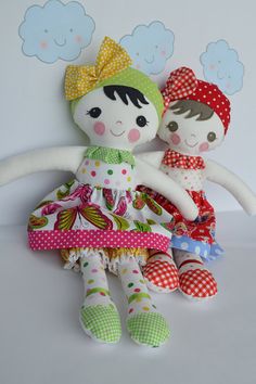 two dolls sitting next to each other in front of a white wall with clouds above them