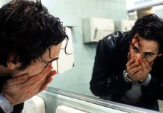 two men are looking in the mirror and one is covering his face with his hands