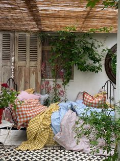 a bed covered in lots of pillows and blankets next to a wall with plants growing on it