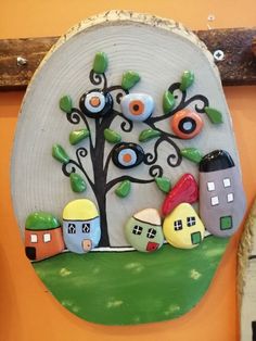 a ceramic wall hanging with houses and trees on the outside, in front of an orange wall