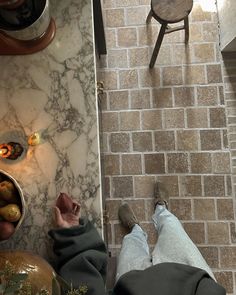 two people standing in front of a brick wall with food on the floor and one person's feet up