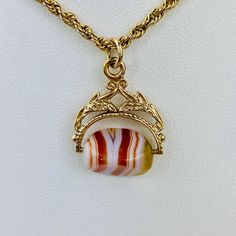 "This is a beautiful Victorian style Swivel Fob Seal / Pendant in 9K / 9ct yellow gold. The spinning fob pendant features hand carved floral gold design and a triangle shaped banded agate with vibrant white, red/orange, and yellow colors. The fob measures 0.87\" (22.3mm) high including bail without split ring and 0.76\" (19.4mm) wide at it is widest point. It is fully hallmarked for Birmingham Assay, 9ct gold, and year letter for 1977. It weighs 3.862 grams. All of our listings come in a box rea Yellow Gold Oval Agate Jewelry, Oval Agate Yellow Gold Jewelry, Oval Yellow Gold Agate Jewelry, Classic Formal Agate Jewelry, Gold Agate Hallmarked Jewelry, Gold Agate Jewelry With Polished Finish, Antique Gold Agate Jewelry, Formal Agate Jewelry With Engraving, Formal Engraved Agate Jewelry