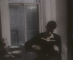 a man sitting at a table with a book in his lap and looking into the window