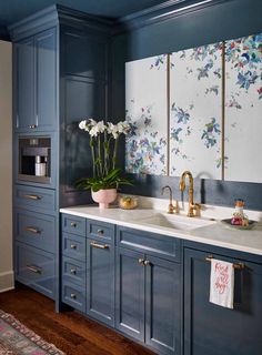 a kitchen with blue cabinets and white flowers on the counter top, along with gold faucets