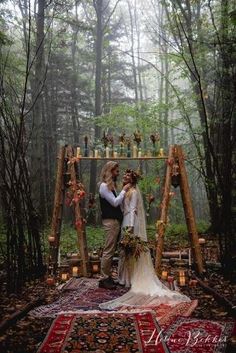 a bride and groom standing in front of a wooden arch with candles on it, surrounded by trees