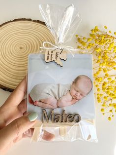 a person holding up a card with a baby's photo on it next to some yellow flowers