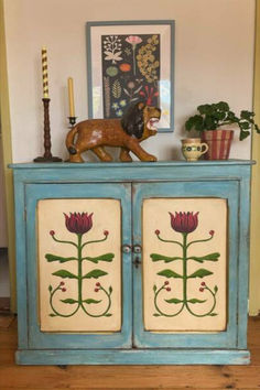 a blue cabinet with flowers painted on the front and sides, next to a candle holder