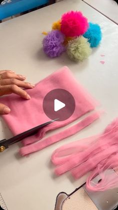 a person cutting fabric with scissors on a table next to pom - poms