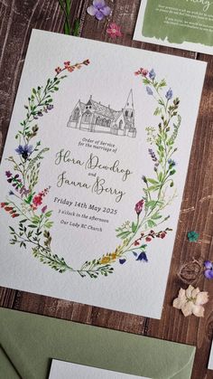 the wedding stationery is laid out on a wooden table with flowers and greenery