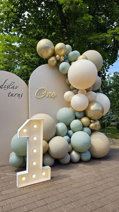 a large number one sign sitting next to a white and gold balloon arch with balloons all over it