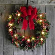 a christmas wreath with red bows and lights hanging on a wooden wall next to a door