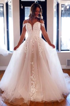 a woman in a white wedding dress standing on a wooden floor with her hands behind her back