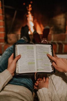 two people sitting in front of a fireplace holding an open book with words on it