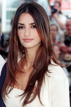 a woman with long brown hair standing in front of a group of people at an event