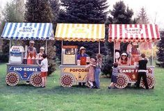 some people are standing in front of an ice cream cart that is decorated with candy bars and striped awnings