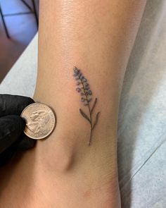 a small lavender flower tattoo on the right side of the ankle by a dime penny