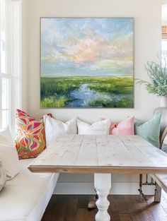 a painting hanging on the wall above a wooden table in a room with white couches