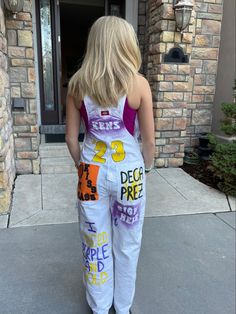 a woman in white overalls with colorful letters on the bottom and sides, standing outside