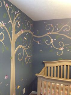 a baby's room with a tree painted on the wall and a crib