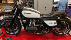 a white and black motorcycle parked on top of a red platform in a garage next to shelves