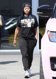 a woman walking down the street wearing black pants and a t - shirt with pictures on it