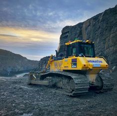 a large yellow bulldozer sitting on top of a dirt field next to a mountain