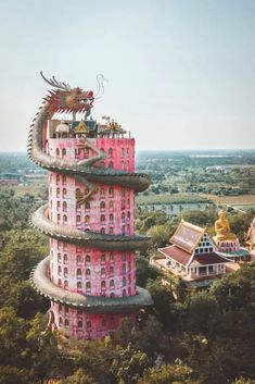 a tall pink building with a dragon on it's roof in the middle of trees