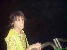 a young man wearing a yellow shirt standing next to a metal hand rail at night