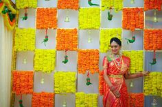 a woman standing in front of a wall with orange and yellow flowers on it's sides