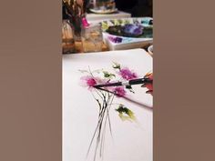 someone is painting flowers on a piece of paper with watercolors in the background