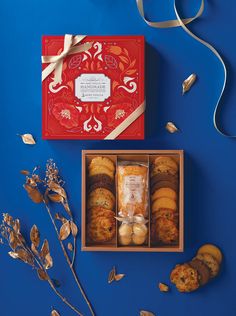 an assortment of cookies in a red gift box with ribbon and flowers on blue background