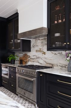 a kitchen with marble counter tops and black cabinets, gold pulls on the oven hood