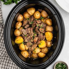 a crock pot filled with beef and potatoes next to a small bowl of parsley