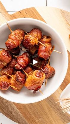 a white bowl filled with bacon wrapped in toothpicks on top of a wooden cutting board