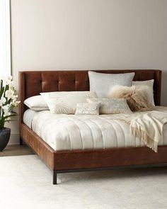 a bed with white and brown pillows in a room next to a plant on the floor