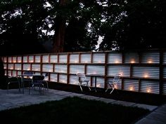 a fence that has lights on it and some chairs in the grass near by at night