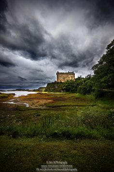 an old castle sitting on top of a lush green hillside under a cloudy sky with dark clouds